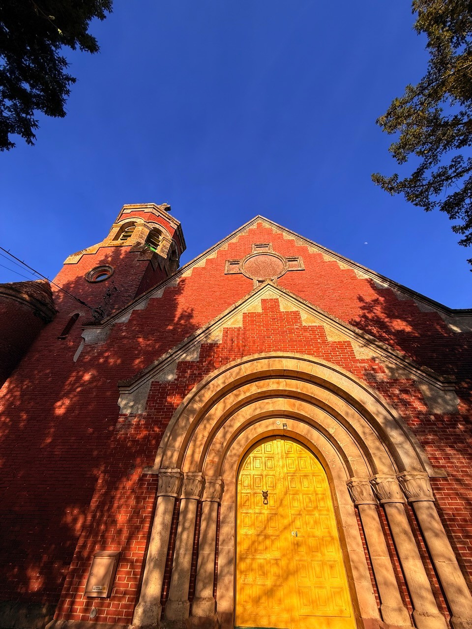 La façade de briques de l’église et sa porte principale peinte en jaune, sous un ciel bleu